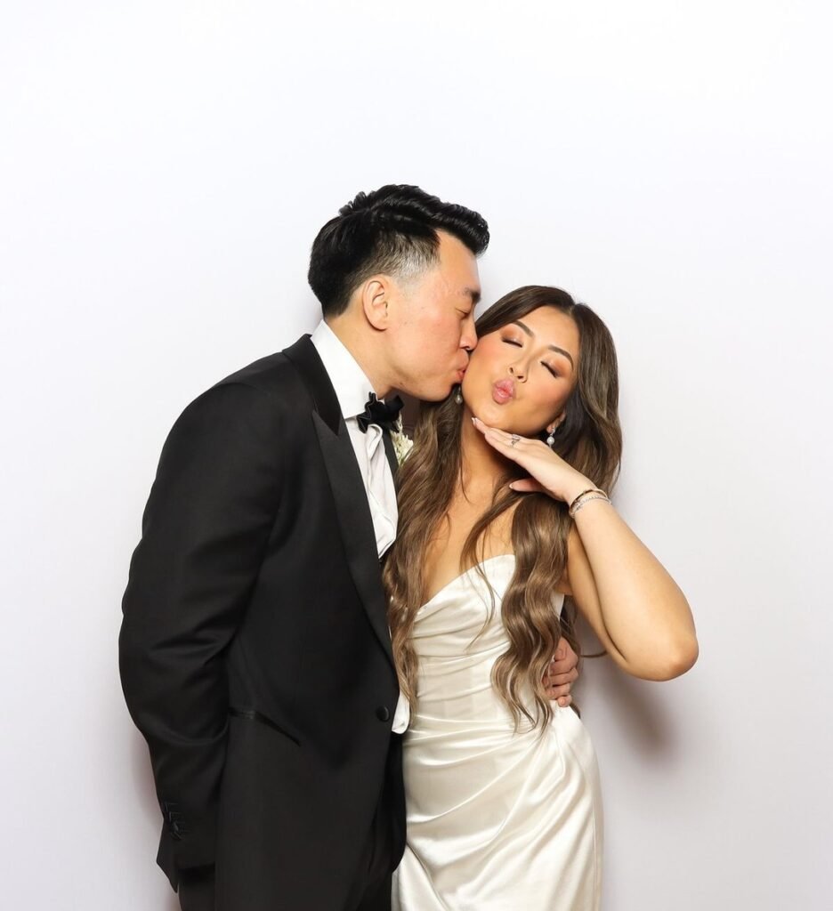Wedding couple posing at a photo booth in front of a white backdrop