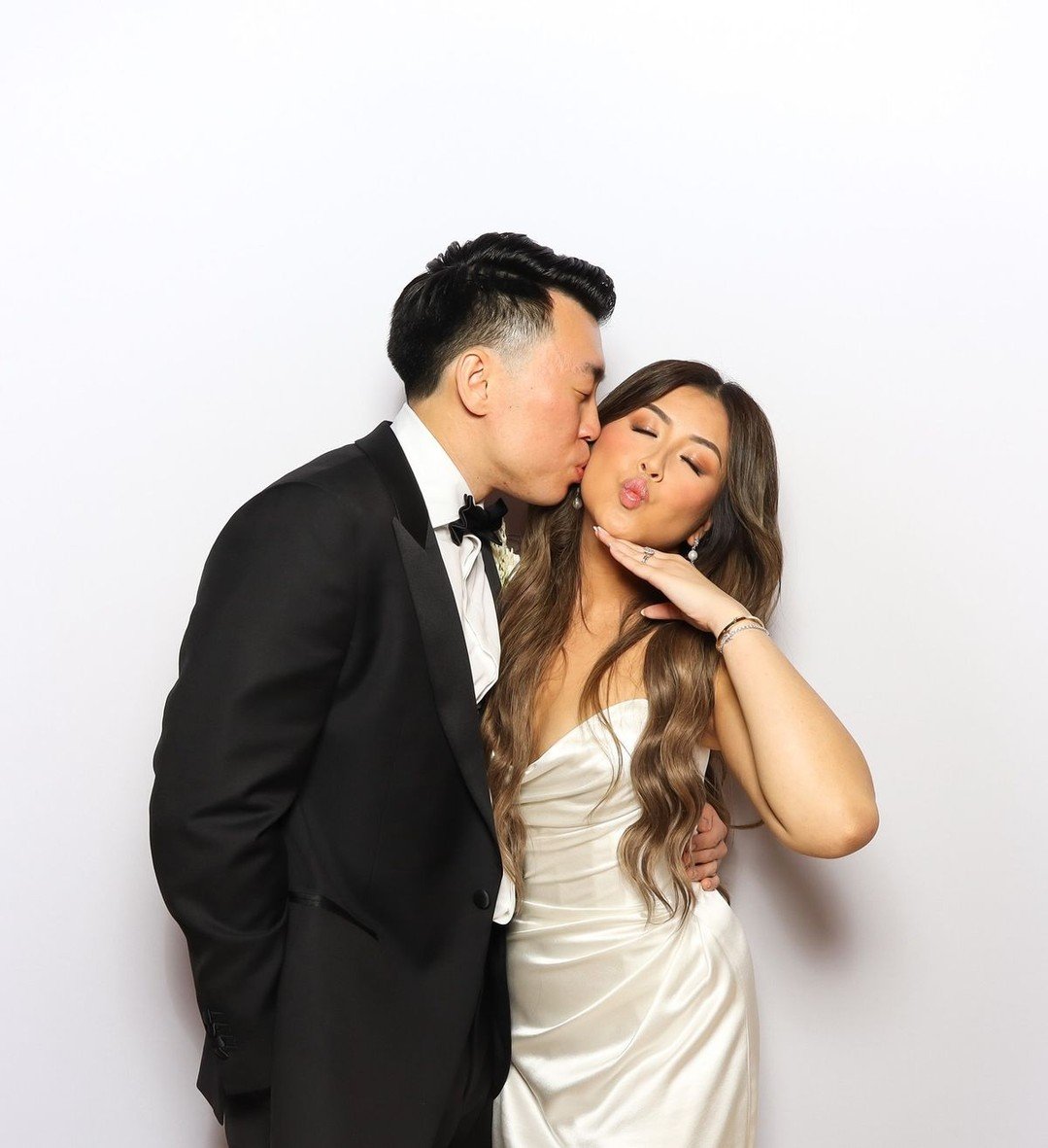 Wedding couple posing at a photo booth in front of a white backdrop